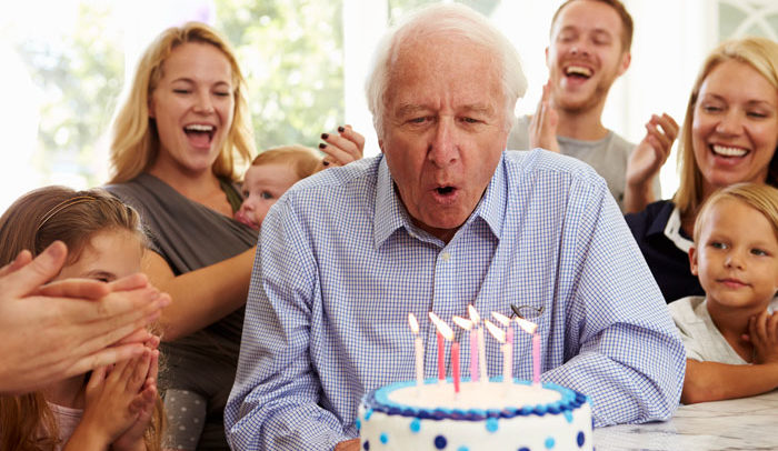 grandfather blowing out birthday cake candles at a birthday party with family
