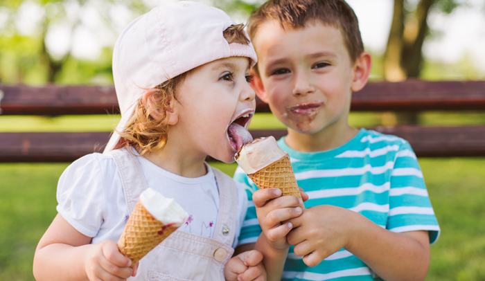 two children sharing ice cream on a park bench