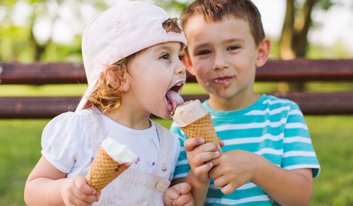two children sharing ice cream on a park bench